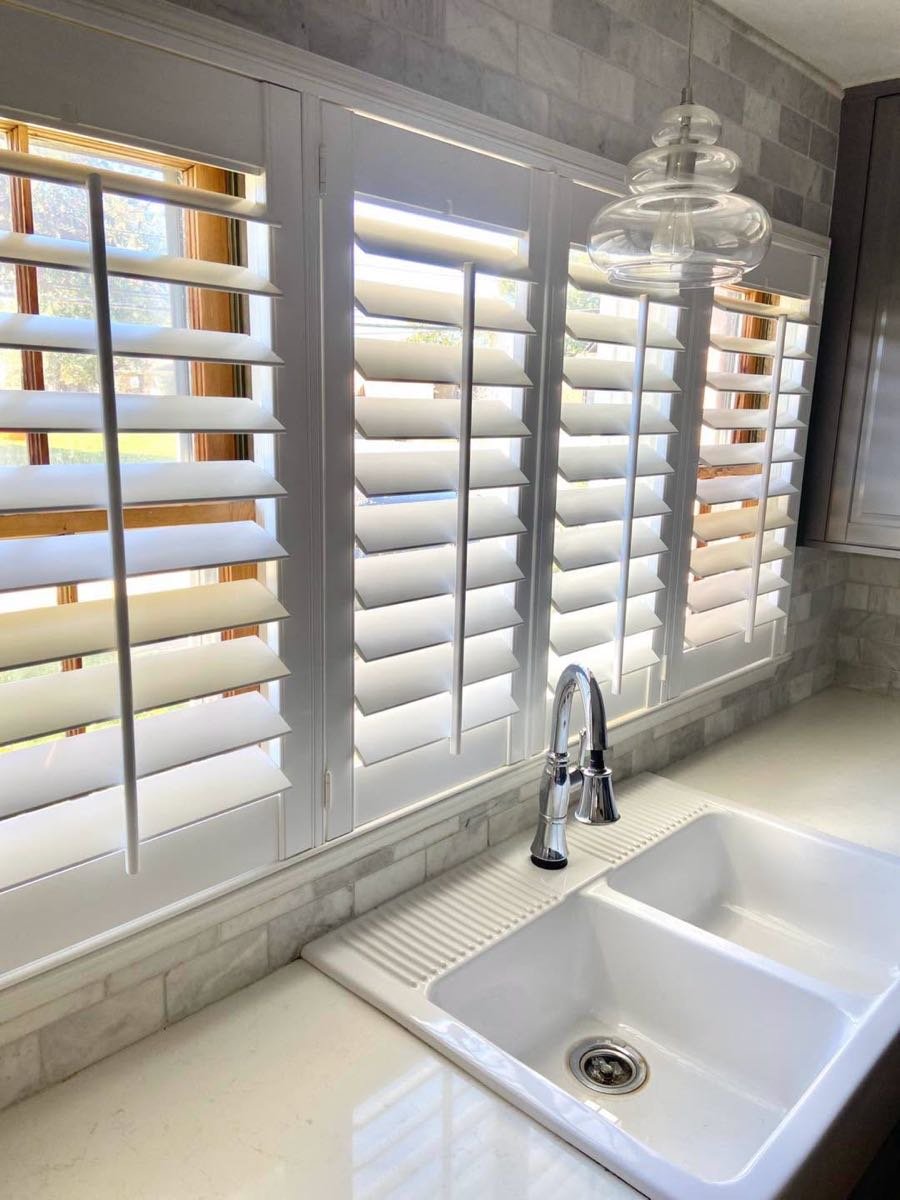 White farmhouse sink under plantation shutters